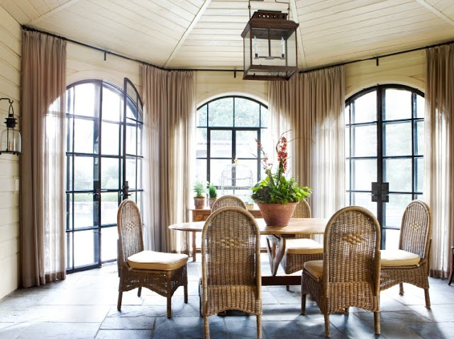 Sunroom with arched windows, a stone floor, wicker dining chairs, a lantern like chandelier and sconces
