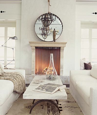living room with dueling sofas, a marble top coffee table separating them, a fireplace with a round mirror on the mantel reflecting a metal chandelier