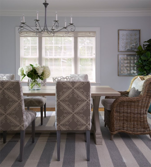 Dining room with a striped grey and white rug, upholstered chairs around a farmhouse style table with a wicker armchair at the head of the table