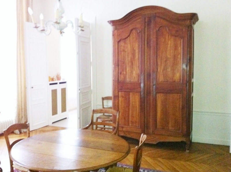 Alternative view of the dining room in the Paris apartment with a view of the large wood cabinet, herringbone wood floor and white double doors leading to the kitchen