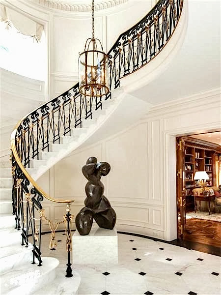 Grand foyer in a Palm Beach estate with marble floor, a large modern sculpture and winding staircase with gold and black railing
