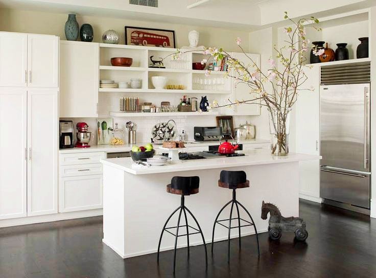 Sleek kitchen with white cabinets and drawers, a dark wood floor, stainless appliances and open shelves holding different kinds of bowls, books and other objects