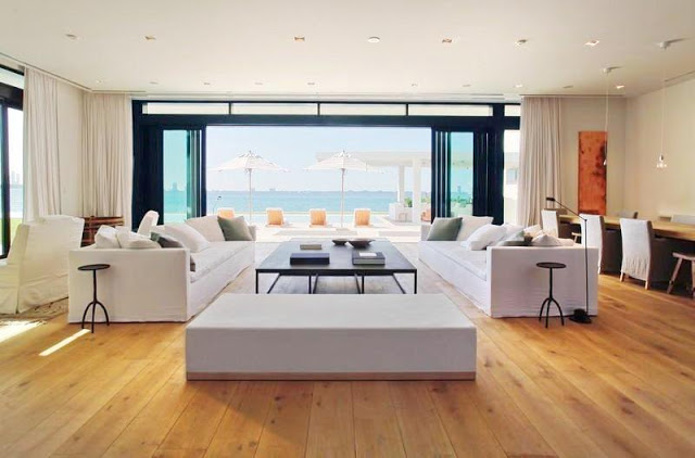 living room with wood floors, white dueling sofas, floor length white curtains, with a large window overlooking the water