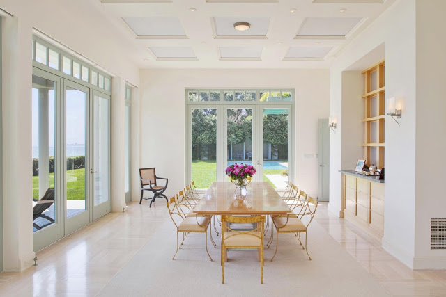 open plan dining room with yellow metal chair surrounding a wood table, high ceilings and windows that offer fantastic views of the pool in the backyard as well as the ocean