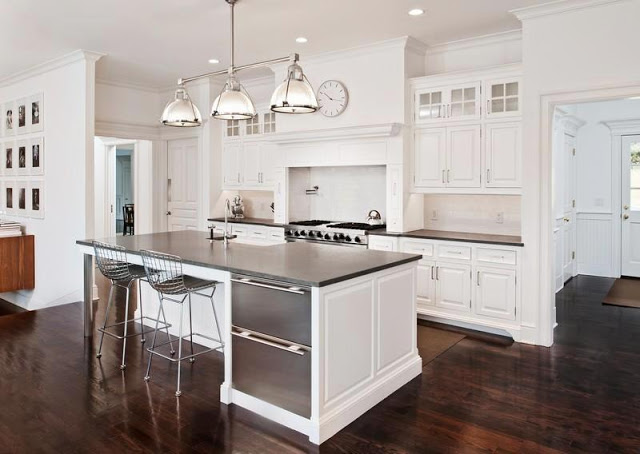 white kitchen in a mansion with dark wood floors, an island, wire chairs, stainless appliances and a pendant style chandelier