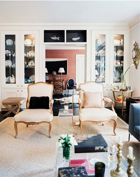 Living room with dark floor, Lucite coffee table, two upholstered Louis XIV chairs and white cabinets with glass doors