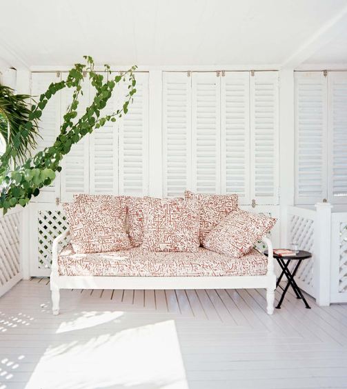 White porch with a black side table and a white daybed with red and white patterned cushions and pillows
