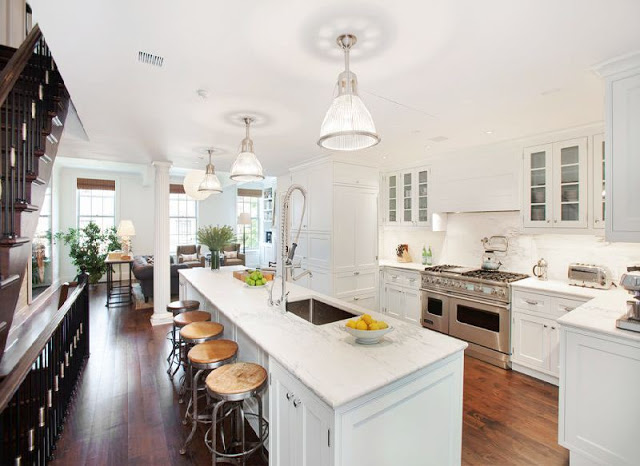open kitchen with marble counters, stainless steel appliances, an island with metal barstools and stained wood floor