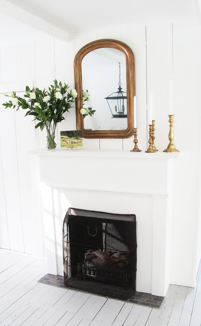 a country farmhouse ktichen fireplace white floors, louis mirror mantel, brass candlesticks, candle and a bouquet