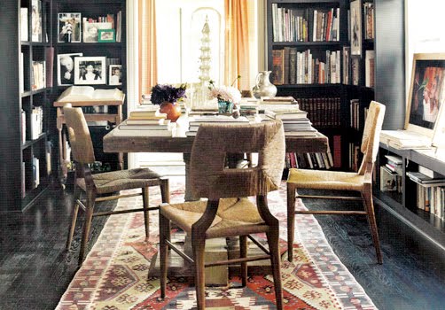 Home office with built in dark wood bookcases and matching dark wood floors, a reclaimed wood table surrounded by rope chairs on a patterned area rug
