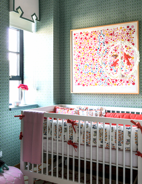nursery with white crib with white bedding with an orange and blue pattern. The walls are covered in a green, triangle print wallpaper with a piece of modern art made of different colored dots on the wall. 