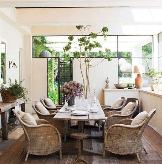 covered enclosed sun porch in t.v. star Ellen Degeneres' home with a rustic dining table surrounded by wicker arm chairs. 