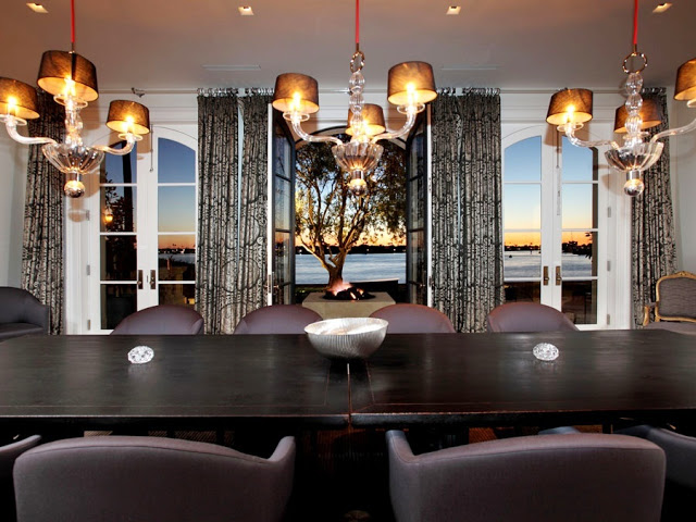 dining room with view of the sunset over the ocean, three crystal chandelier light fixtures, a long dark table with leather seats