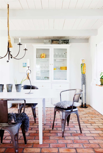 Metal cafe chairs with furry modern cushions surround a traditional white farmhouse table in the home's dining area which also as a chandelier and white glass door cabinet
