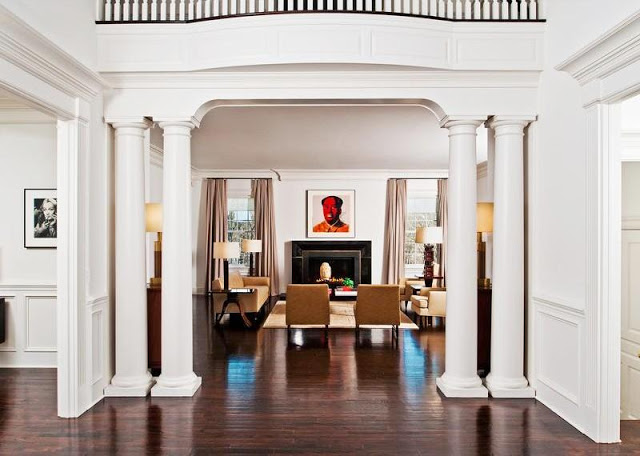 foyer in a mansion with white columns and a wood floor with a view into the living room 