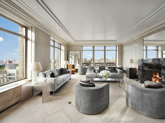 Living room in a NYC penthouse with light wood herringbone floor, grey sofas and armchairs and a marble fireplace mantel 