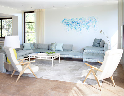 Alternative view of a pastel living room with a sectional sofa, two armchairs with wood legs and arms, large windows and a painted graphic mural of varied shades of blue dots