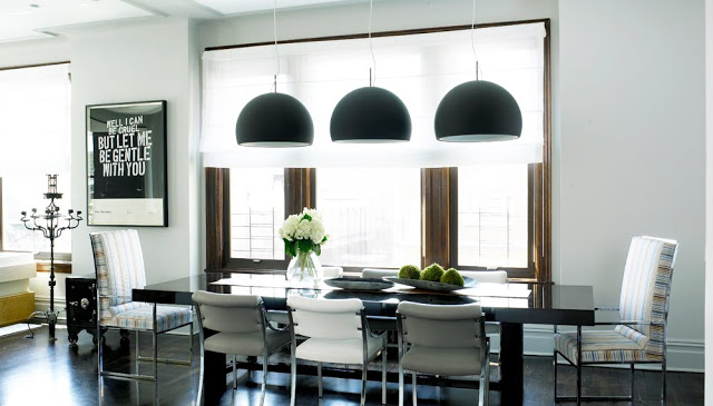 Sleek modern kitchen with three black dome pendant lights hung over a black dining room table surrounded by upholstered chairs with higher back chairs at the head of the table. 