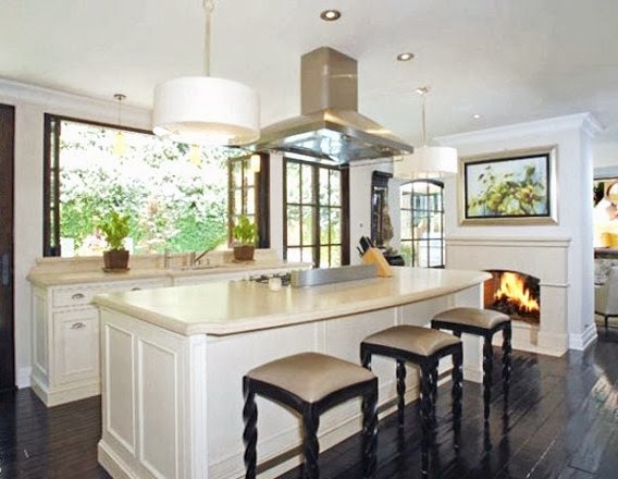 Kim Kardashian's kitchen with dark wood floors, wood bar stools, white pendant lights and a fireplace