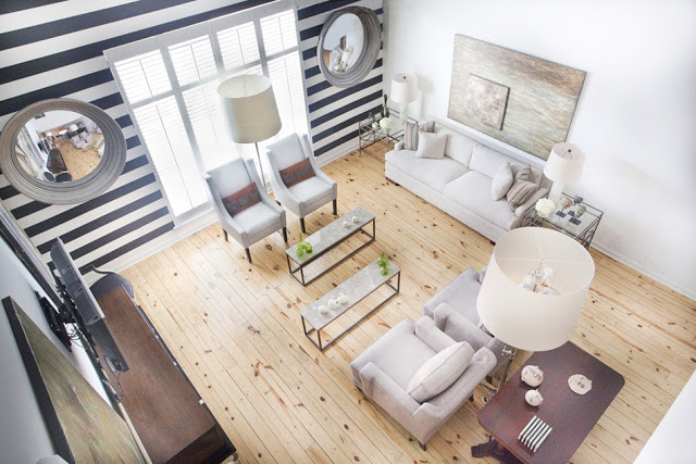 bird's eye view of a living room with knotty wood floors, striped black and white wall with two accent windows, white sofa with matching armchairs and glass coffee tables