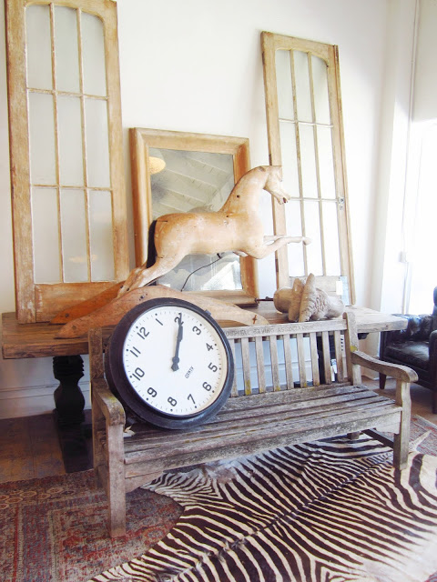 Brenda Antin store in Los Angeles with a reclaimed wood bench with a large clock sitting on it, zebra skin rug, a wood horse, windows