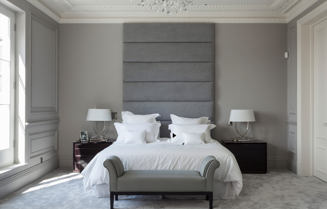 Grey bedroom in a suburban London home with a tall upholstered headboard, carved crown moulding, and light grey carpet