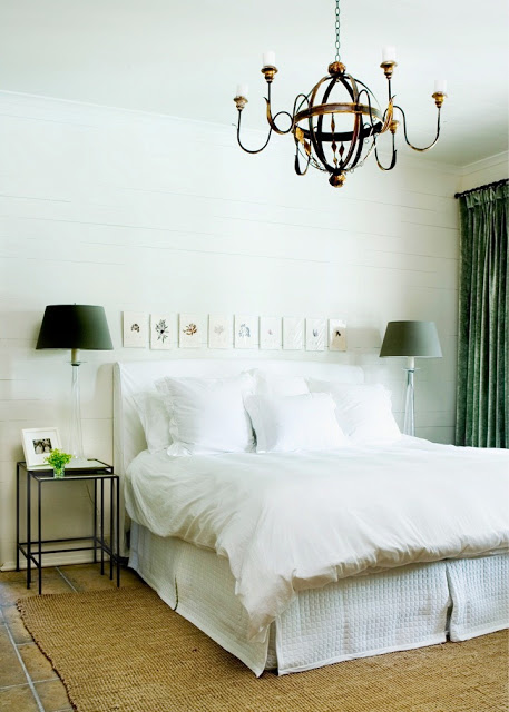 Bedroom with a white slipcovered headboard, green floor length curtains, tile floor and a brass chandelier