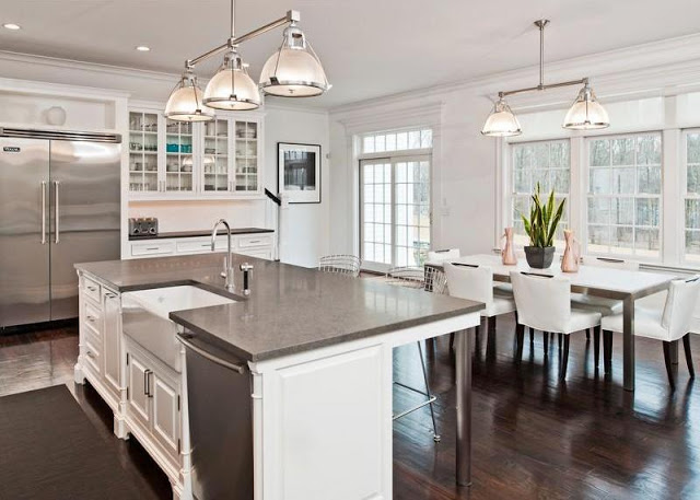 white, dine in kitchen in a mansion with french doors and windows, dark wood floors, a pendant style chandelier, and white upholstered chairs surrounding a dark wood rectangle table