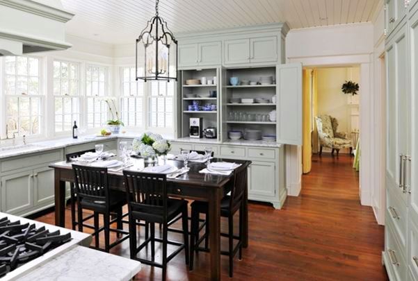 Alternative view of the kitchen and its grey cabinets, marble counter tops, casement windows, stained oak table dining room table surrounded by matching chairs and a chandelier