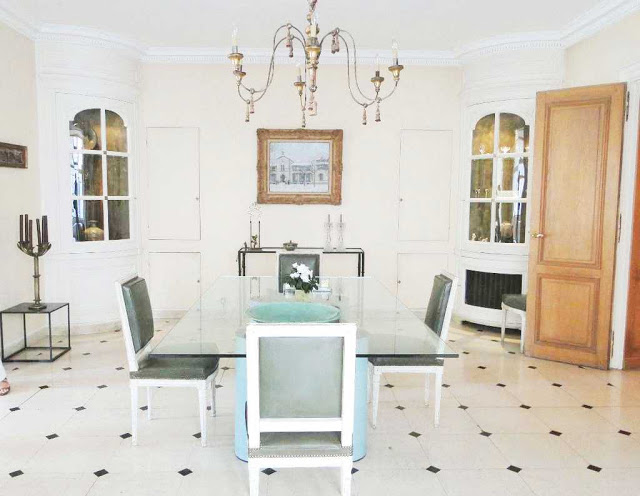 Dining room in a Paris apartment with a glass table, louis xvi chairs, built in curio cabinets and a white tile floor