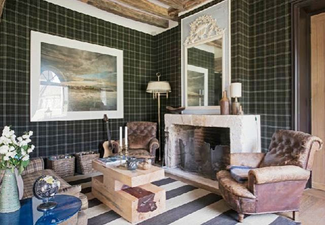 den with plaid walls and a striped rug with exposed beams, leather chairs, fireplace with a trumeau mirror on the mantel