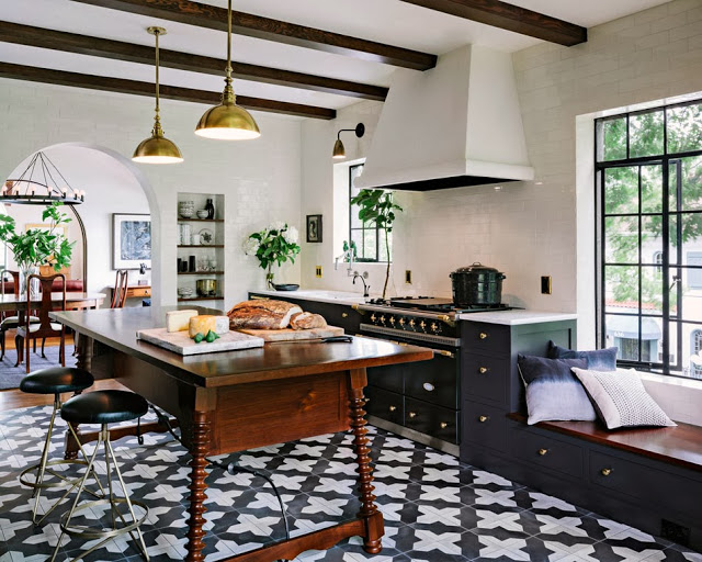 Modern kitchen with a counter height antique wood table with turned legs acting as an island, cement tile floor, and brass pendant lights