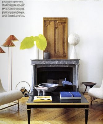 Living room with herringbone wood floor, a marble fireplace, and a black lacquer coffee table. On the table is a Yves Klein blue book