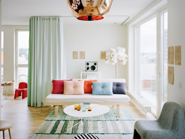living room with mint green floor length curtains, copper tom dixon pendant, green and white striped rugs, wood floor, white sofa and brightly colored pillows