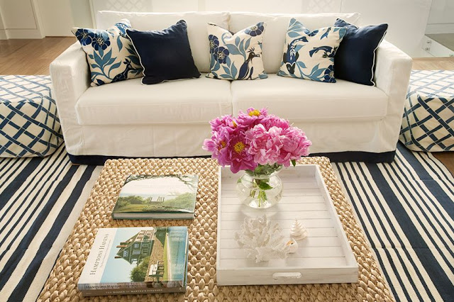 living room with blue and white striped rug, white couch with navy and bird printed accent pillows, two ottomans with blue trellis acting like side tables, and a woven ottoman coffee table