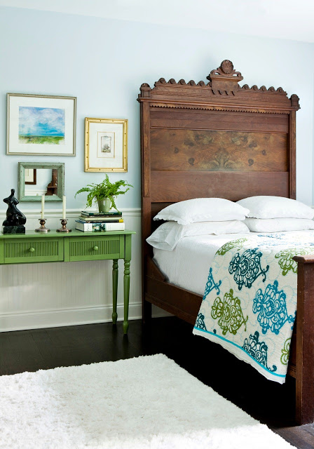 Bedrooom with antique wood headboard, green night stand, wood floors and a white rug
