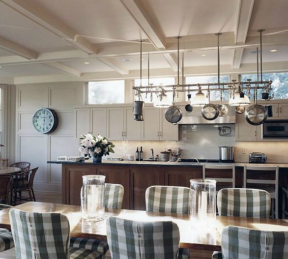Dine in kitchen with hanging pot rack, white cabinets, a wood island with slab counter top, and a long wood table with gingham seat covers