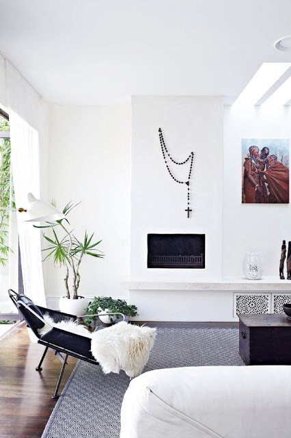 Living room with white washed walls with prayer beads as wall hanging, fireplace, dark wood floor and a patterned rug