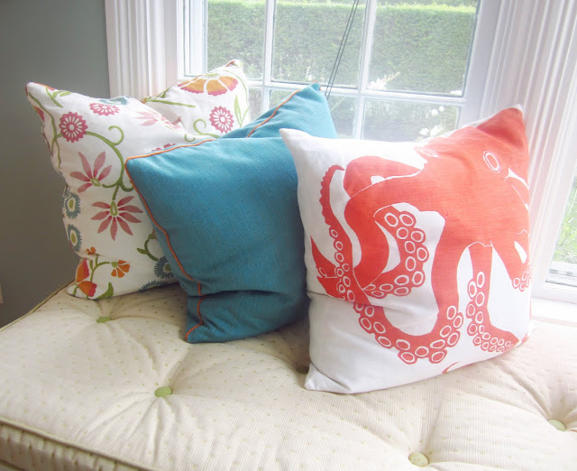 three decorative pillows on an upholstered cushion in a window seat