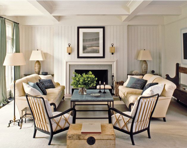 Symmetrical living room with two facing sofas, two matching arm chairs, two matching lamps on either side of the fireplace, and the exact same throw pillows on each sofas, white beadboard walls and a coffered ceiling
