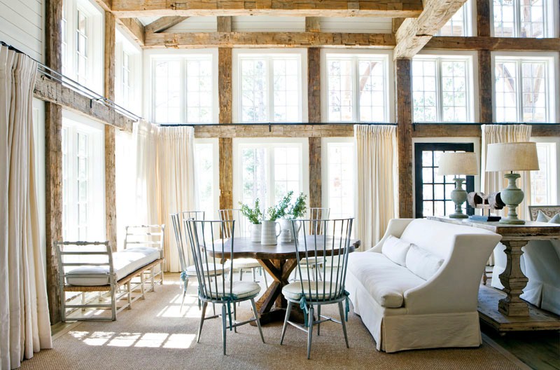 Second seating area in a rustic dining room with high ceiling, exposed reclaimed wood beams, a white sofa, a tree trunk table and light blue metal chairs with white round cushions