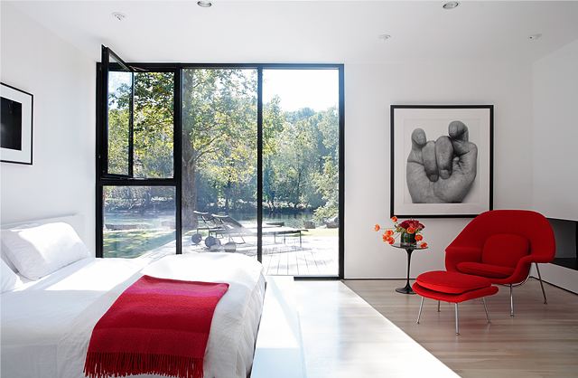 modern bedroom with a encasement window with black trim, wood floor, a red chair and a red throw on a white bed