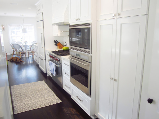 gallery kitchen with stainless steel appliance oven, white panel hood, refridgerator, pantry, dark wood floors with a view of the breakfast nook