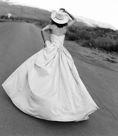 Photo of a woman from behind wearing a strapless wedding runnning and holding a cowboy hat