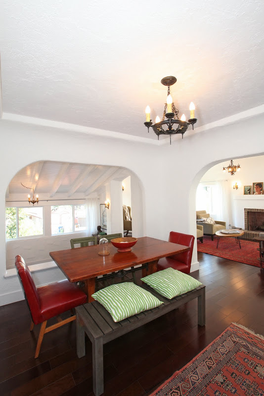 Dining room in a Spanish style home with Koa wood floor, a redwood table with upholstered red leather chairs at the head and foot of the table, a bench with green striped cushions arched entry ways and a Moroccan inspired rug