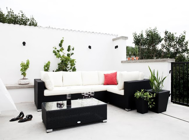 white outdoor patio with black potted plant, coffee table and sofa with white cushions and a view of a backyard