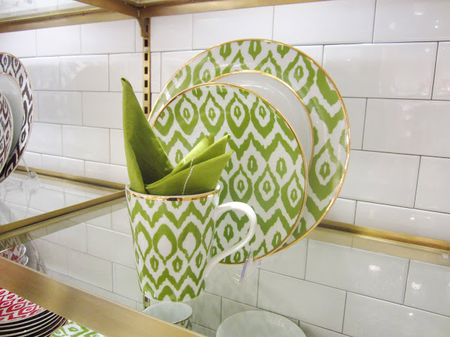 Green and white ethnic print ceramic dish ware on a floating, glass shelf with subway tile walls 