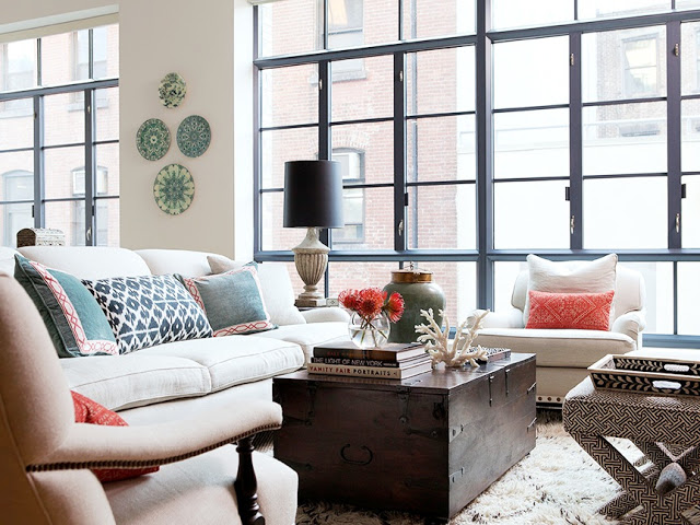 New York apartment with floor to ceiling black trimmed windows, a large trunk serving as a coffee table, white sofa with ikat print pillows, and dueling arms chairs