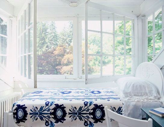 White bedroom with large rustic windows, a wood headboard and blue and white floral bedding