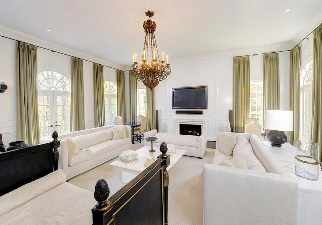 Family room with a wall mounted television, dueling white sofas, a chandelier, and lots of green drapes